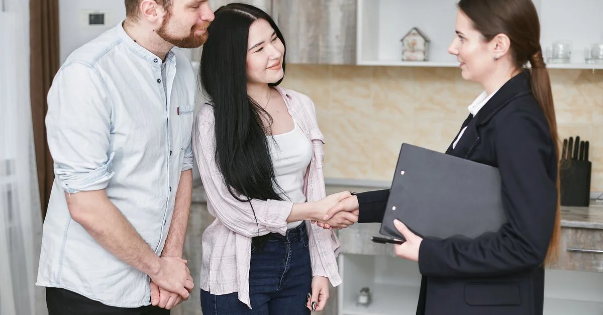 Un jeune couple serre la main d'un agent immobilier lors d'une visite ou négociation dans un cadre moderne.