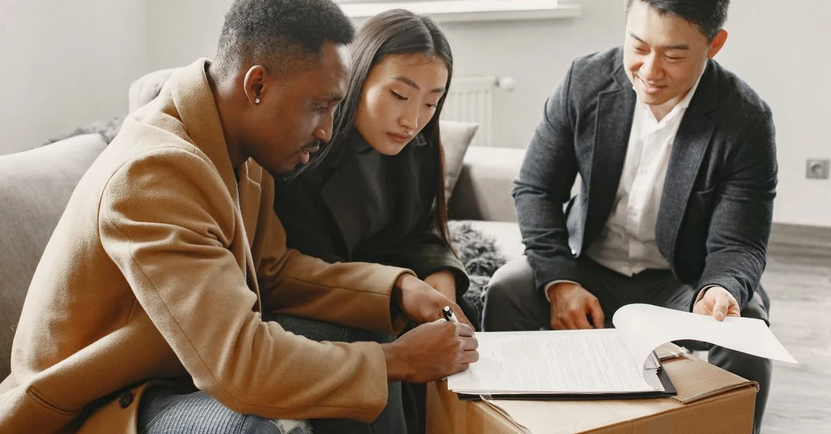 Un couple multiracial signant des documents immobiliers avec un agent dans une maison.