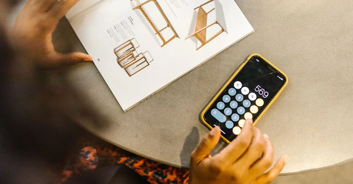 Une personne utilisant une calculatrice sur smartphone à côté d'un magazine ouvert dans un café.