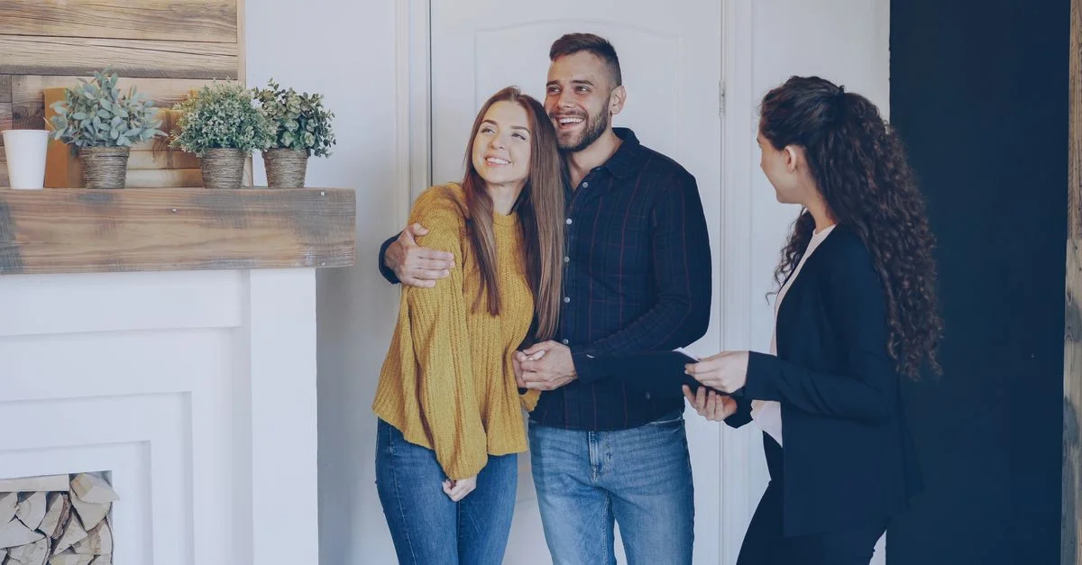 Couple heureux se rencontrant avec un agent immobilier à l'intérieur, discutant de l'achat d'une propriété dans un salon moderne.