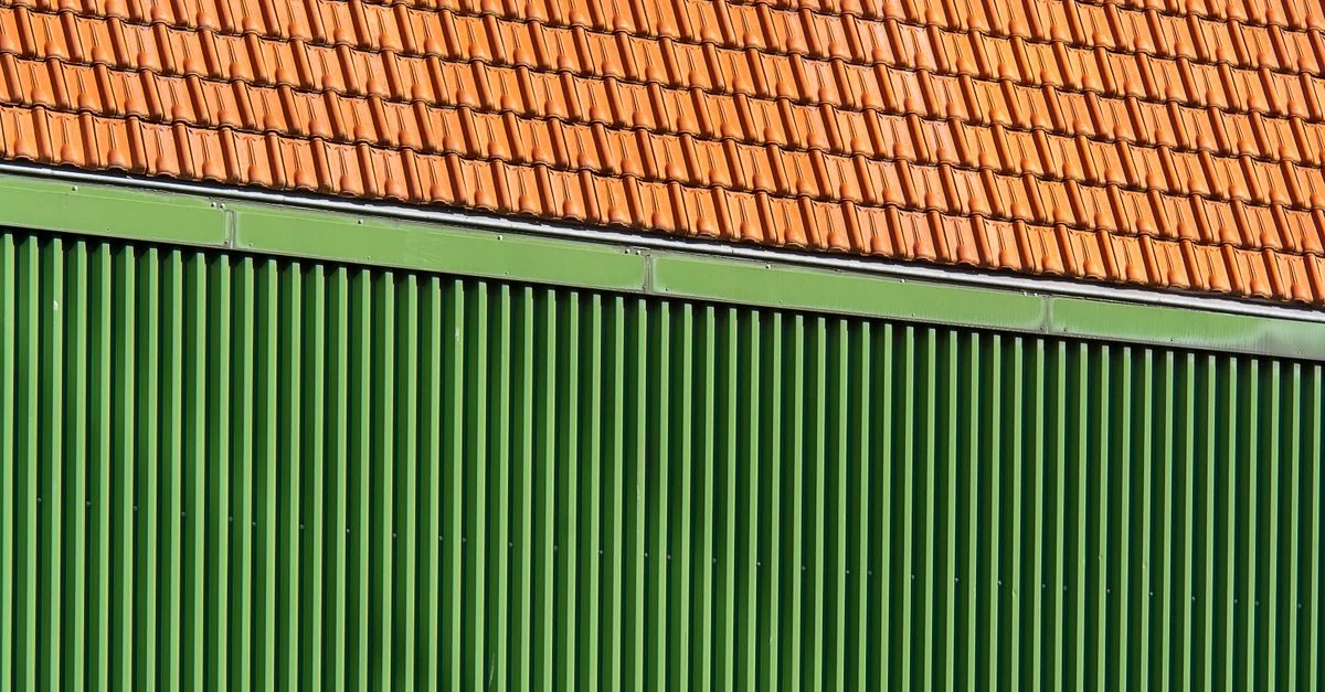 Gros plan de tuiles de toit orange vives et mur ondulé vert.