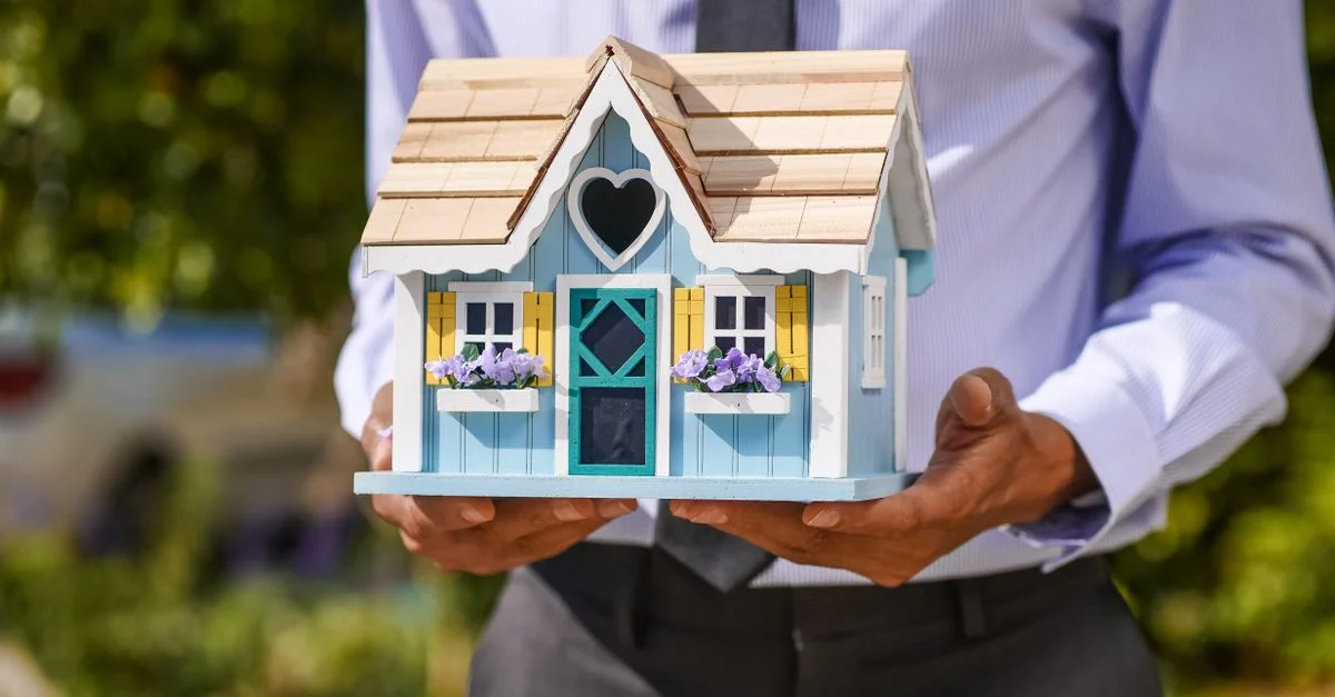 Un homme d'affaires tient un modèle de maison miniature détaillé et coloré. Idéal pour des concepts d'immobilier et d'investissement immobilier.