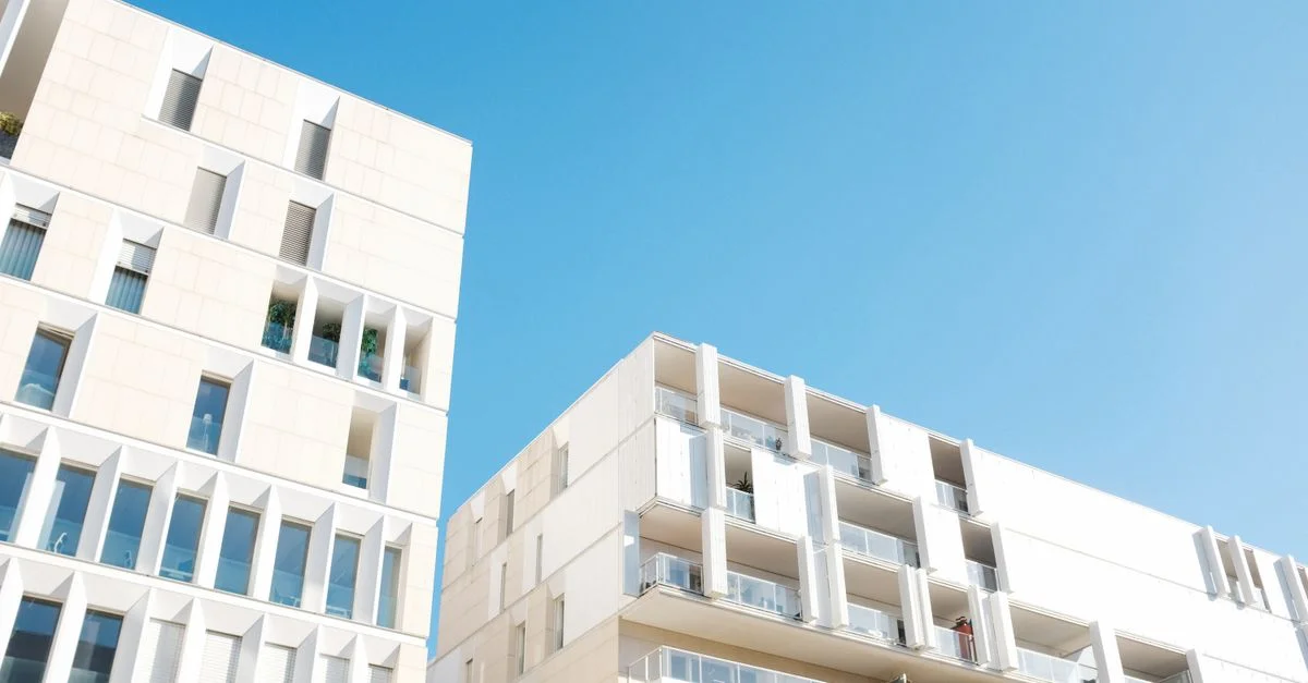Vue en contre-plongée d'un immeuble d'appartements moderne sous un ciel bleu clair, mettant en valeur un design épuré et minimaliste.