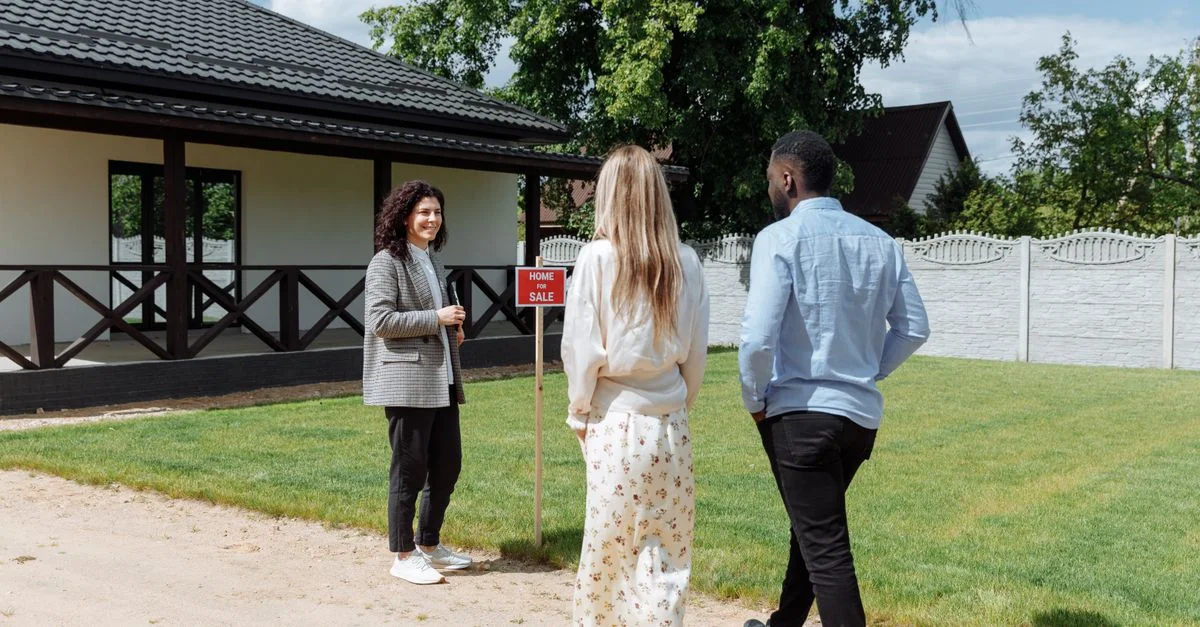 Un groupe divers regardant une maison à vendre avec un agent immobilier à l'extérieur.