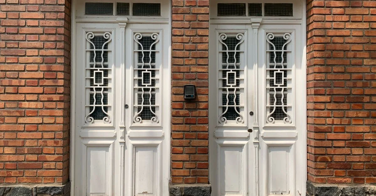 Portes doubles blanches ornées devant une façade en briques rouges avec interphone et numéro de maison 217.