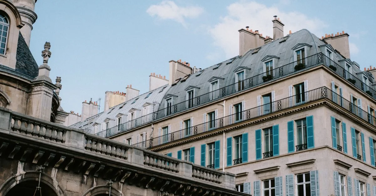 Élégants bâtiments parisiens à l'architecture ornée et volets bleus distinctifs sous un ciel dégagé.