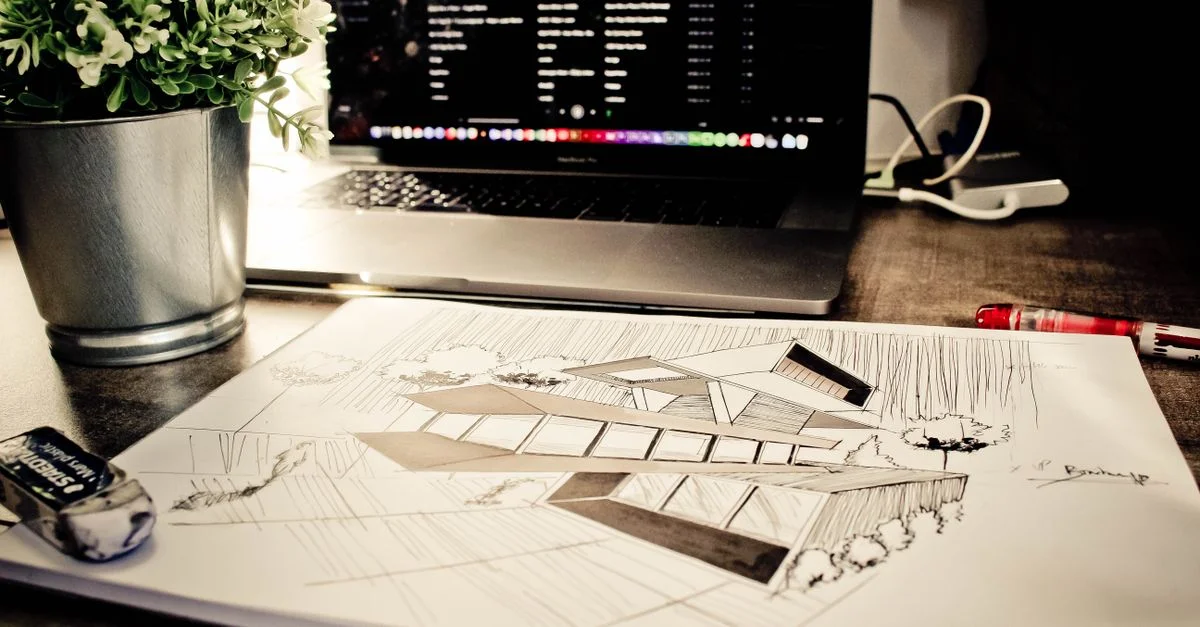 Croquis architectural sur un bureau avec un ordinateur portable et une plante dans un cadre de bureau.