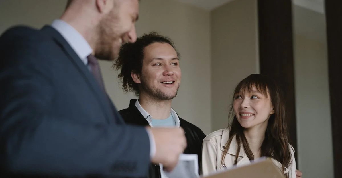 Jeune couple heureux conversant avec un agent immobilier à l'intérieur au sujet d'un nouvel appartement.